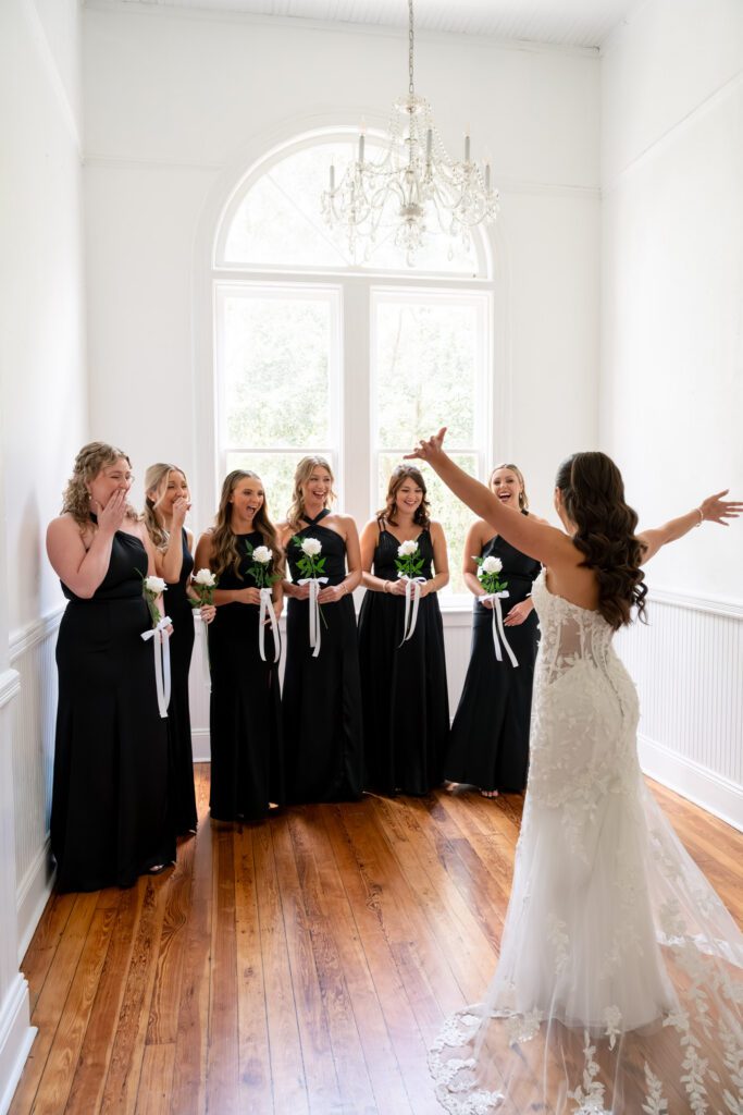 Bride revealing her wedding dress to bridesmaids inside a bright, elegant room with natural light and hardwood floors at a Historic Venue 1902 wedding