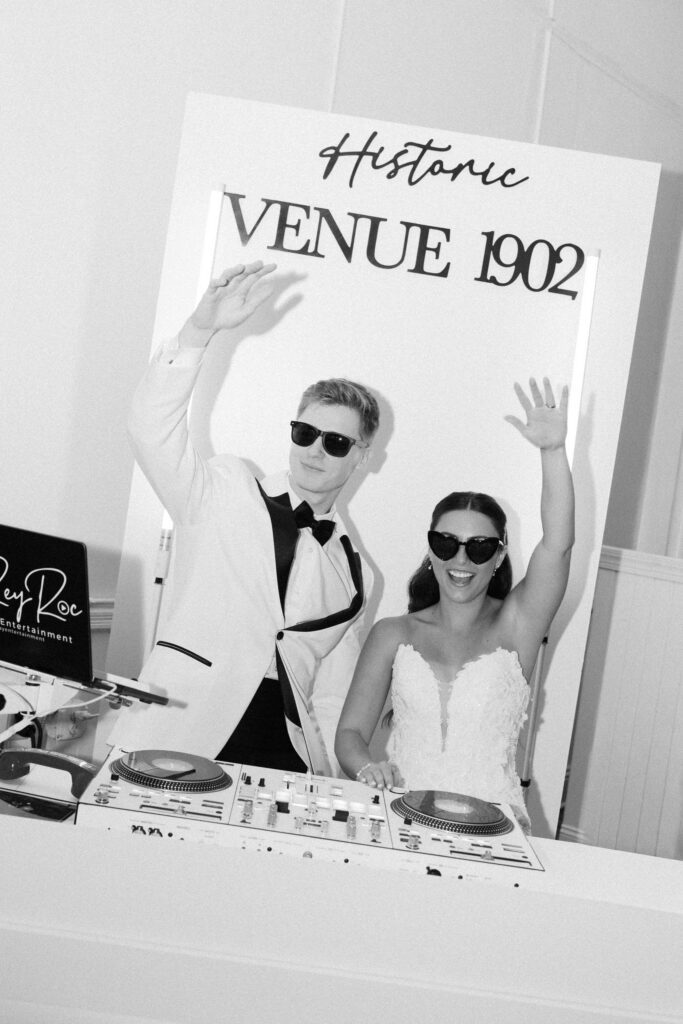 Bride and groom wearing sunglasses and celebrating behind a DJ booth during a fun reception moment at a Historic Venue 1902 wedding in Central Florida