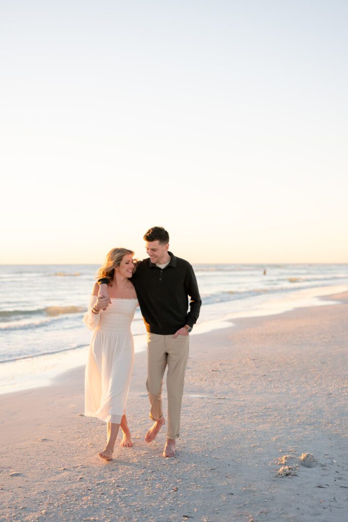 Couple walking barefoot along the shoreline during golden hour Siesta Key Beach engagement photos session on Florida’s Gulf Coast