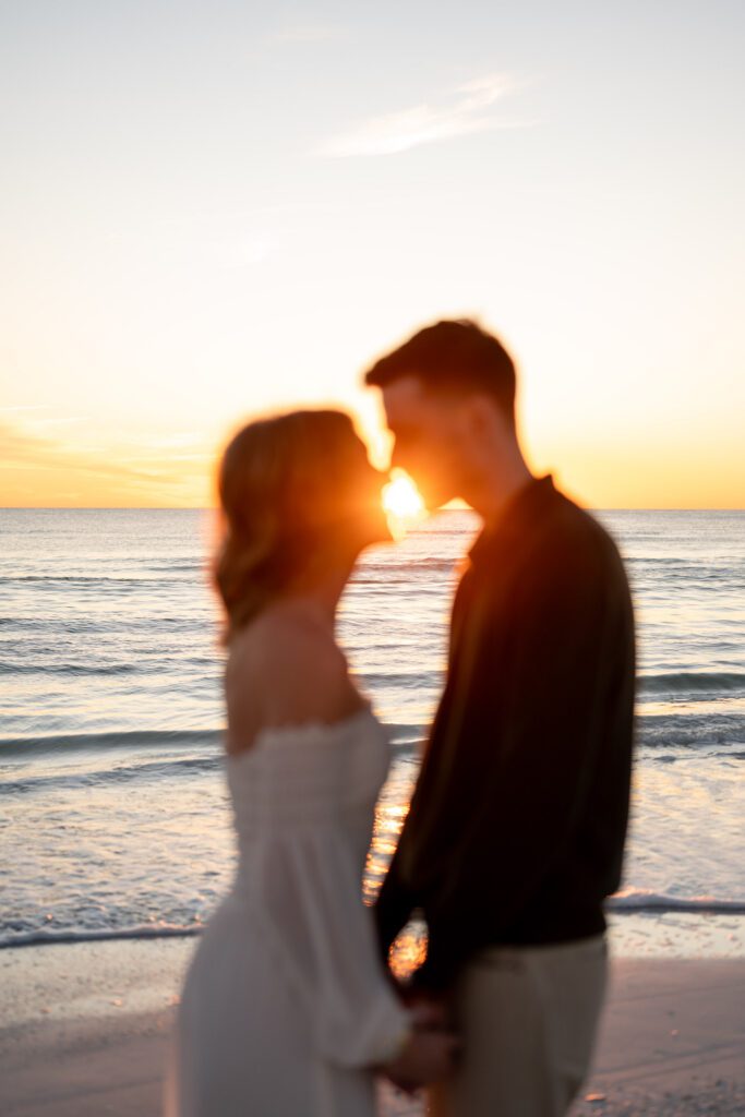 Romantic silhouette of a couple kissing at sunset during their Siesta Key Beach engagement session with golden Gulf Coast light