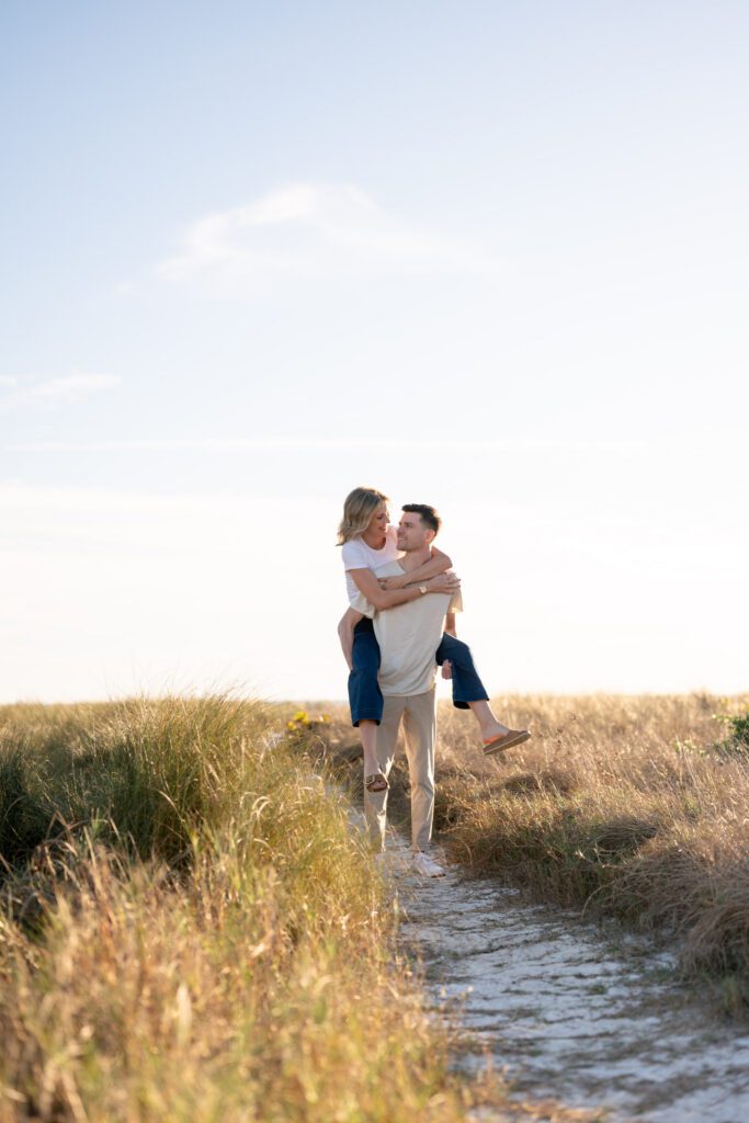 Playful piggyback moment along a sandy path during a Siesta Key Florida engagement session near Sarasota’s coastal dunes