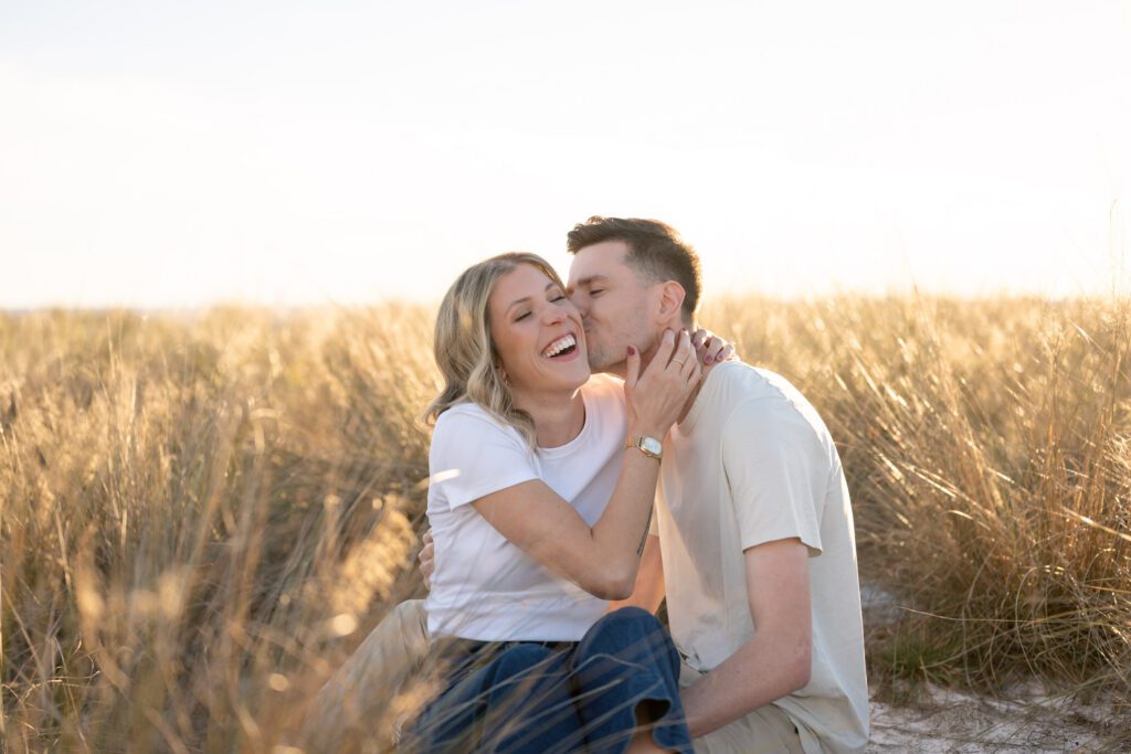 Candid couple laughing together in the dunes during Siesta Key Beach engagement photos with soft golden Sarasota light