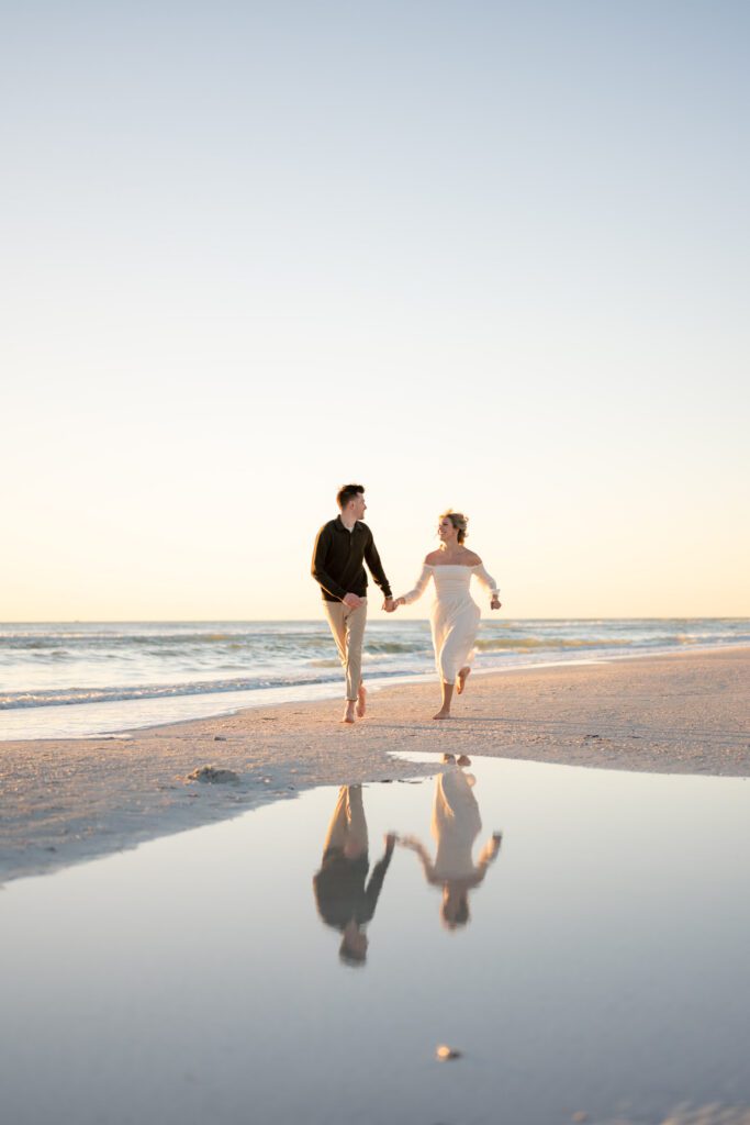 Couple walking hand in hand along the shoreline with reflections in the water during Siesta Key Beach engagement photos at sunset