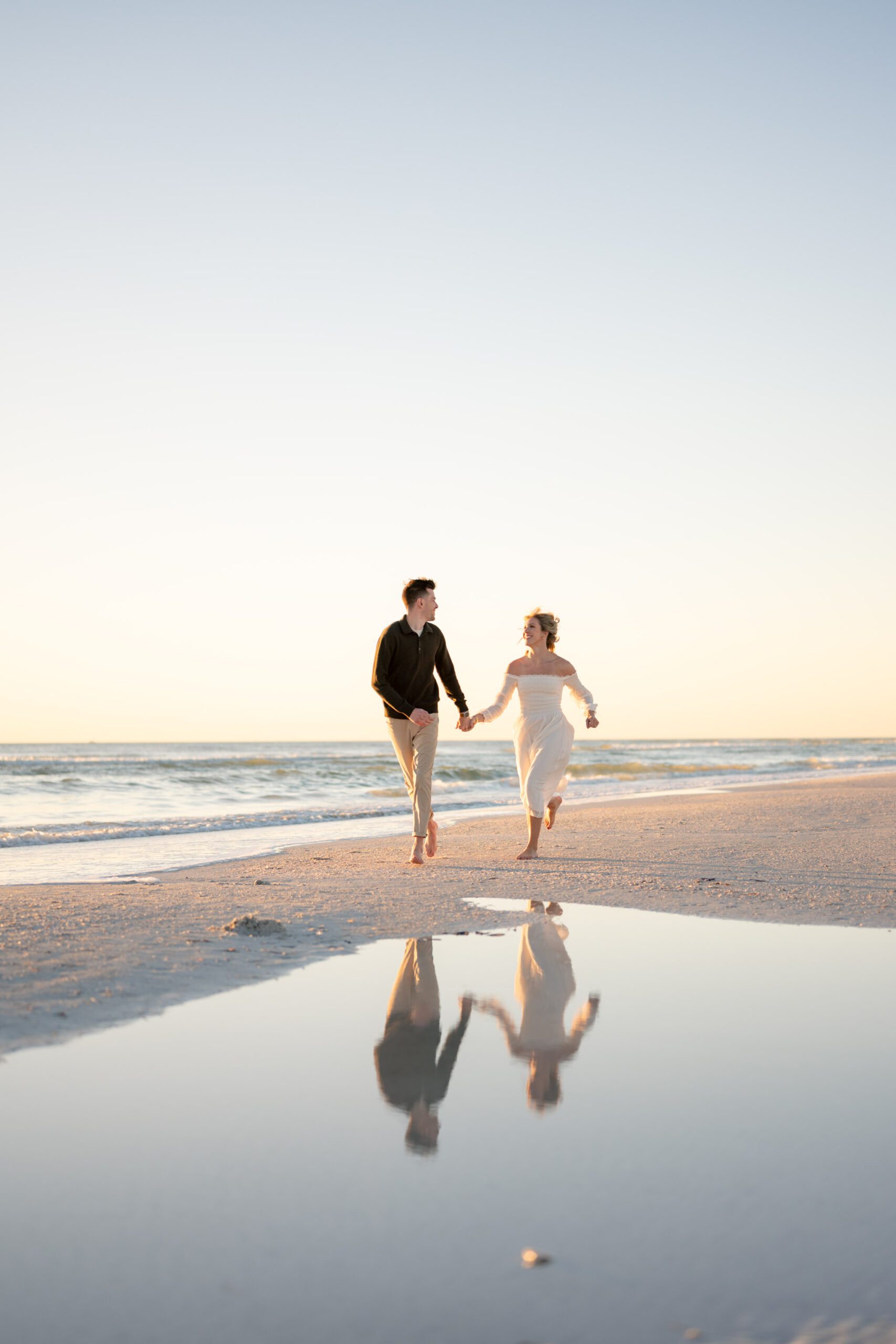 Couple walking hand in hand along the shoreline with reflections in the water during Siesta Key Beach engagement photos at sunset