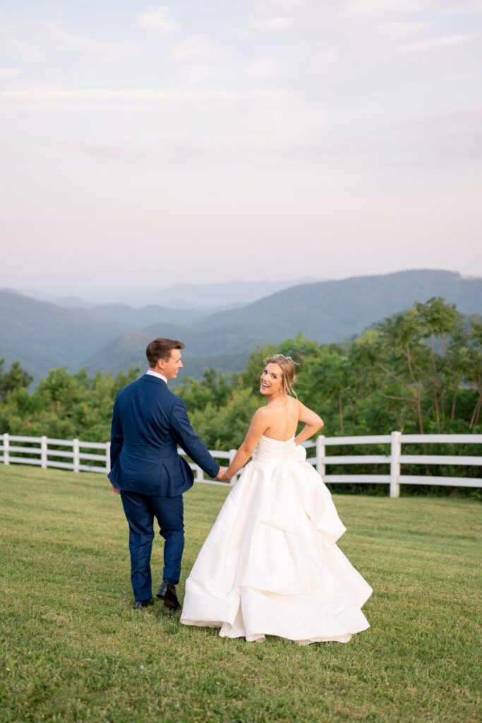 Summit on Cross Mountain wedding with bride and groom walking overlooking Blue Ridge Mountains in Jefferson NC