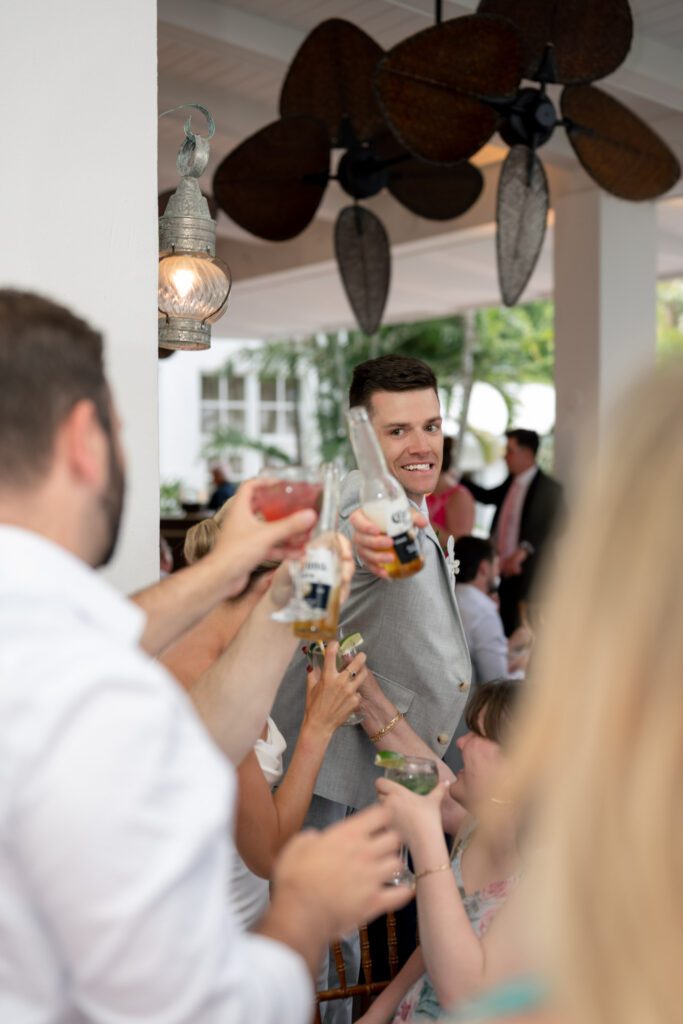 Groom raising a drink and toasting with guests during a lively indoor reception with tropical details at The Palms Hotel & Spa wedding