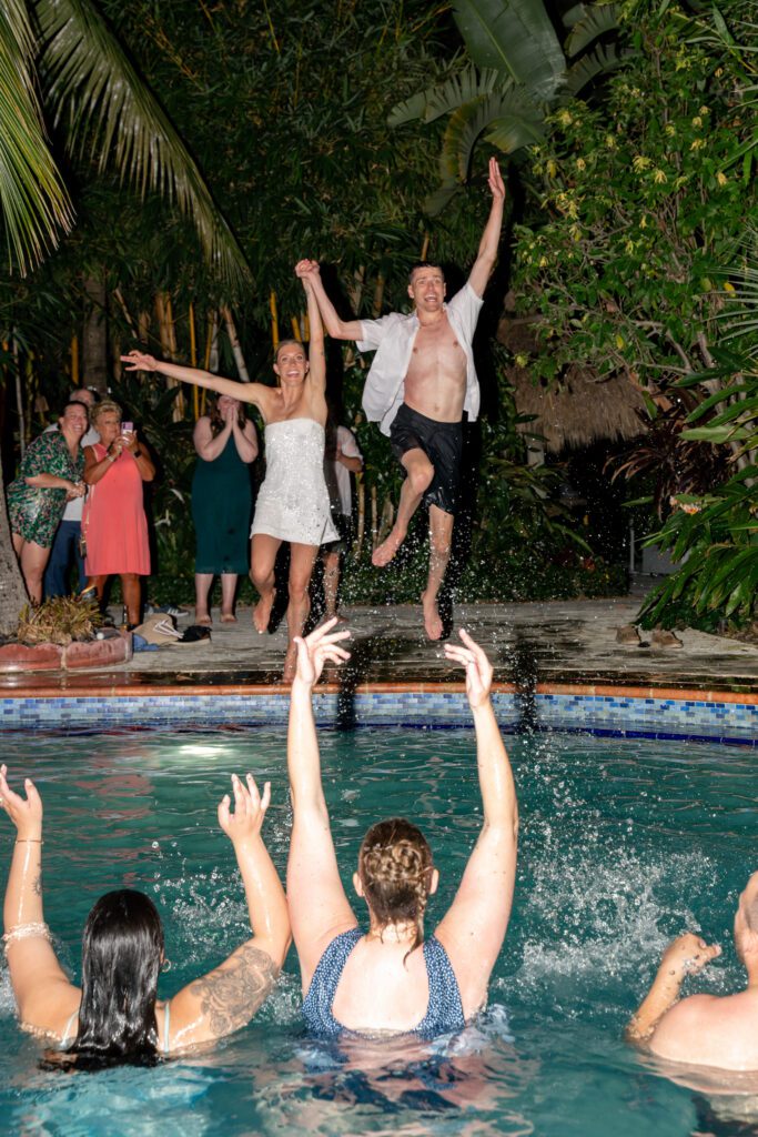 Bride and groom jumping into a pool with guests cheering during a fun, high-energy reception moment at a Miami Beach destination wedding