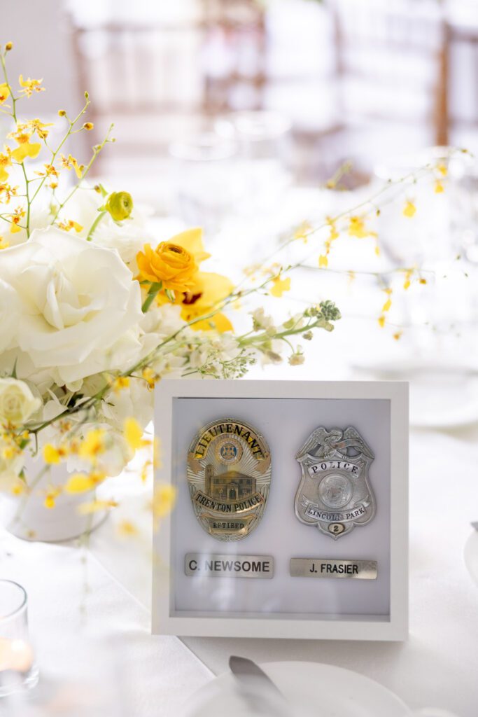 Reception table detail featuring floral arrangements and a framed display of memorial badges honoring loved ones during an elegant celebration at The Palms Hotel Miami Beach wedding venue