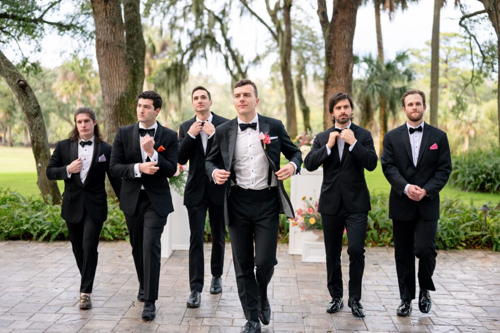 Groom and groomsmen walking confidently together in black tuxedos during a stylish outdoor portrait captured by a Space Coast wedding photographer