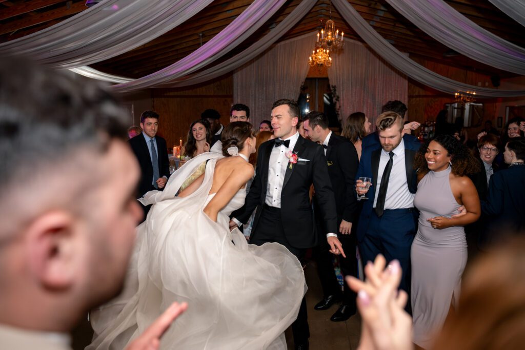 Bride and groom dancing together under draped ceilings and chandeliers during a lively reception at an Up The Creek Farms wedding