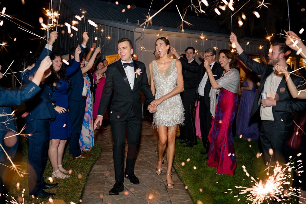 Bride and groom walking through a sparkler send-off surrounded by cheering guests during a joyful evening exit at an Up The Creek Farms Melbourne FL wedding