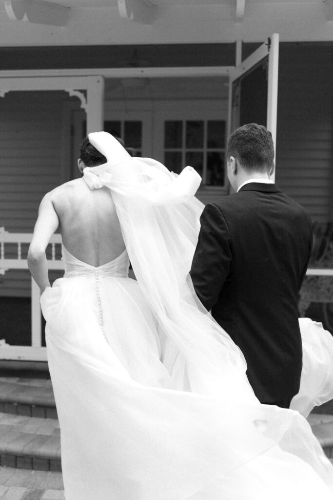 Bride and groom walking up the steps together with a flowing veil, captured in a timeless black and white moment at an Up The Creek Farms wedding