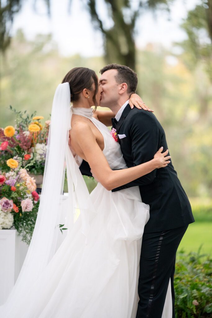 Couple sharing a kiss at the altar surrounded by vibrant floral arrangements and soft greenery at an Up The Creek Farms Melbourne FL wedding