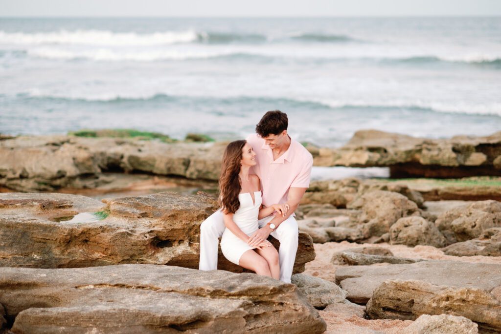 Romantic couple seated on coquina rocks during Washington Oaks Gardens State Park engagement photos along the Palm Coast shoreline