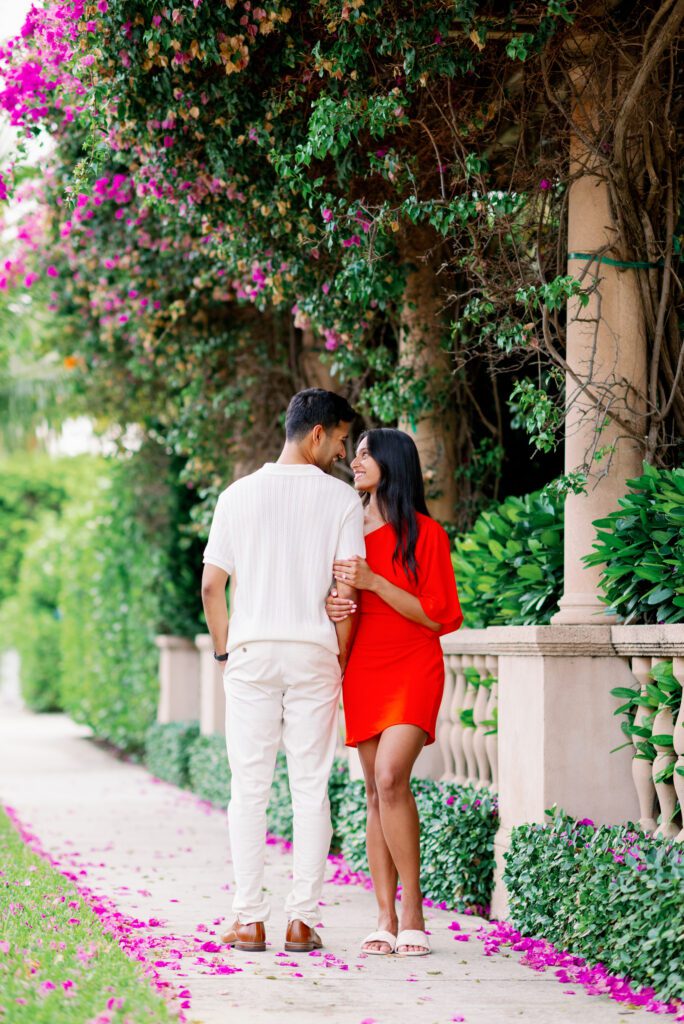 Romantic couple walking through a lush garden pathway during a Palm Beach engagement session with vibrant florals along Worth Avenue