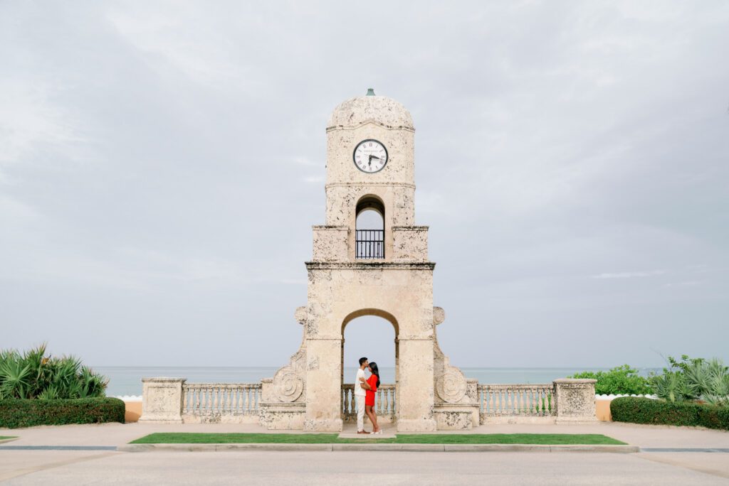 Couple standing beneath the Worth Avenue Clock Tower in Palm Beach, Florida following a romantic Worth Avenue Clock Tower proposal with ocean backdrop