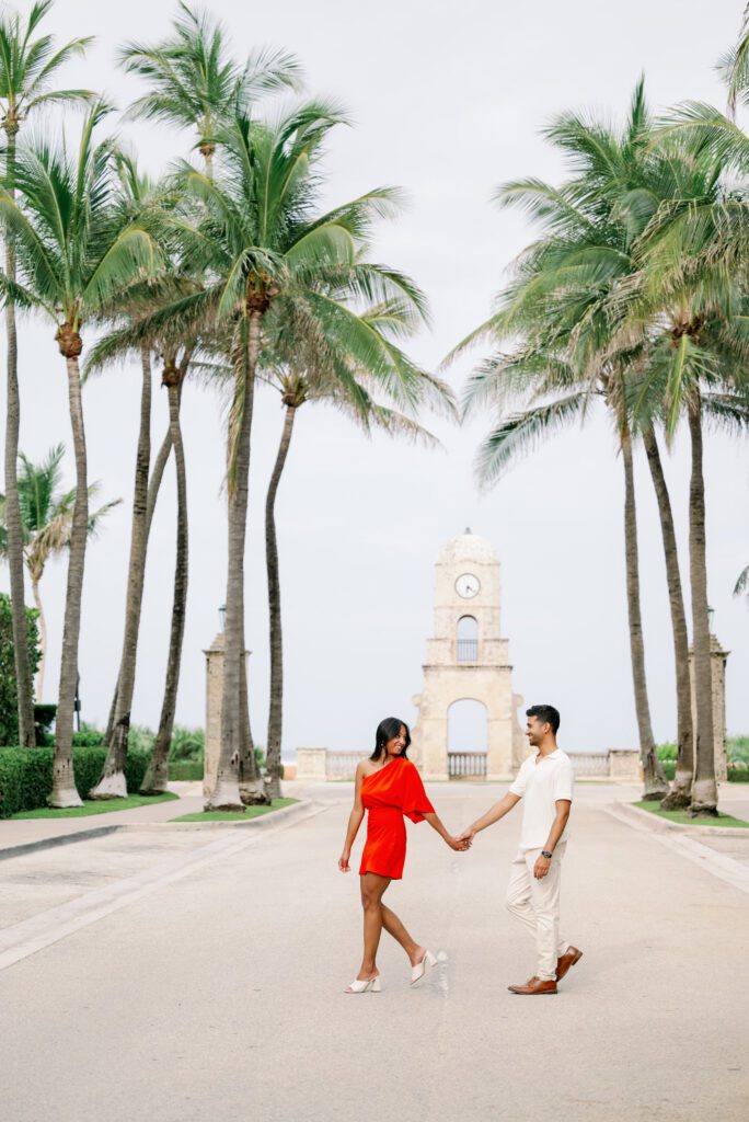Couple walking hand in hand toward the Worth Avenue Clock Tower during a Palm Beach engagement session with iconic palm-lined street views